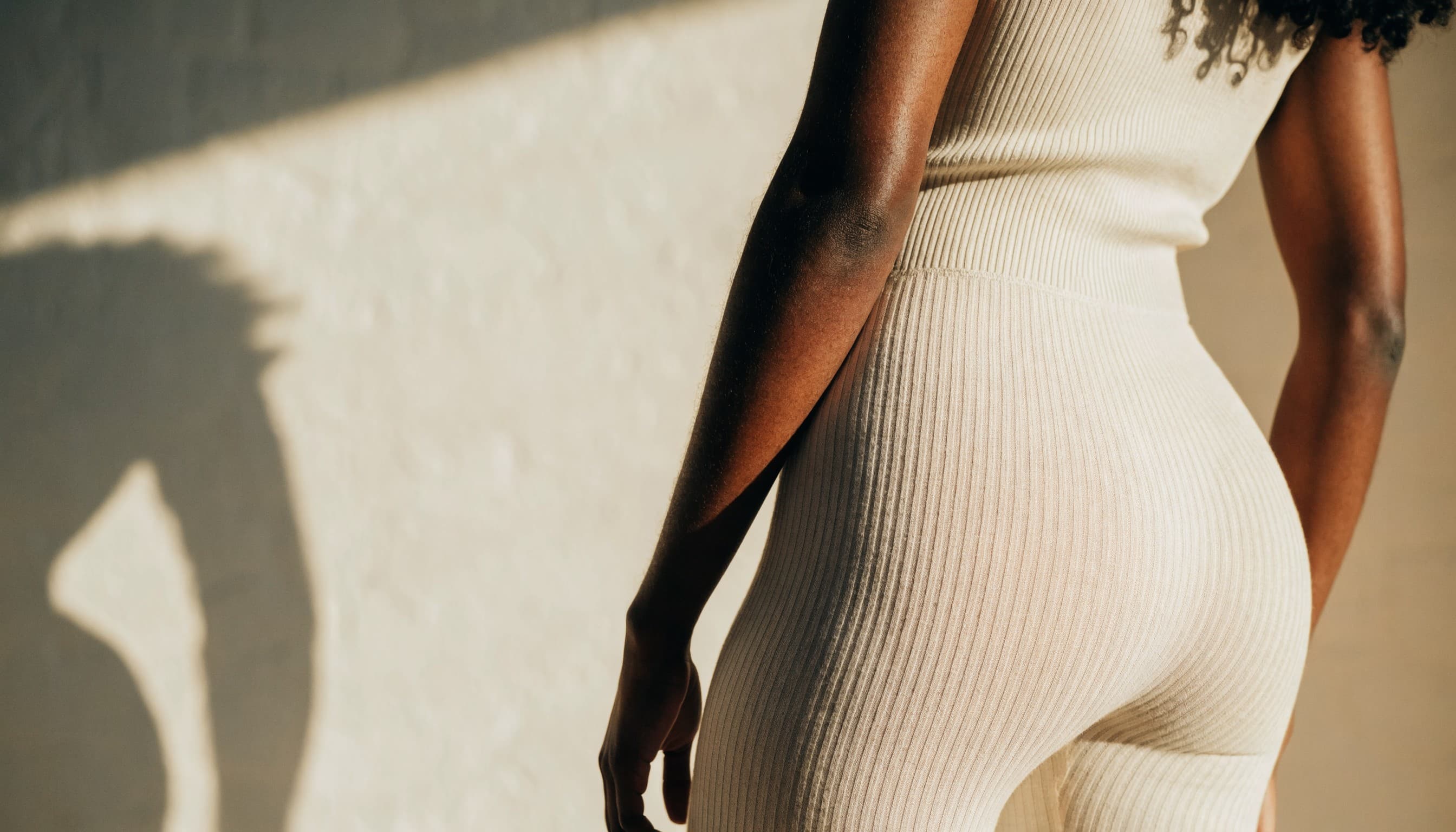 A client in a cream ribbed set, photographed from behind in warm daylight
